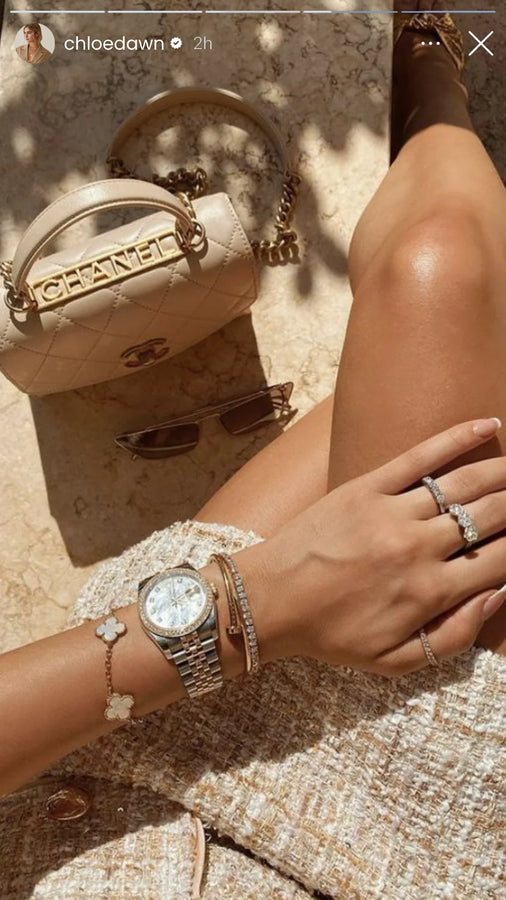 Gold clover jewelry and watch beside a quilted handbag