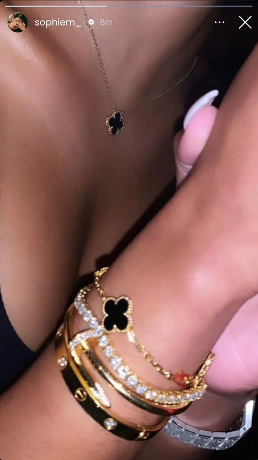 Black clover pendant and layered bracelets on a wrist