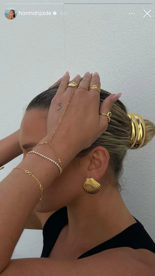Gold shell earring and layered bracelets on a woman with a bun
